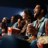 Cheerful man having fun while watching movie with friends in cinema.