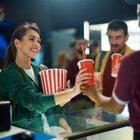 Young happy woman buying drinks and snacks in movie theater.